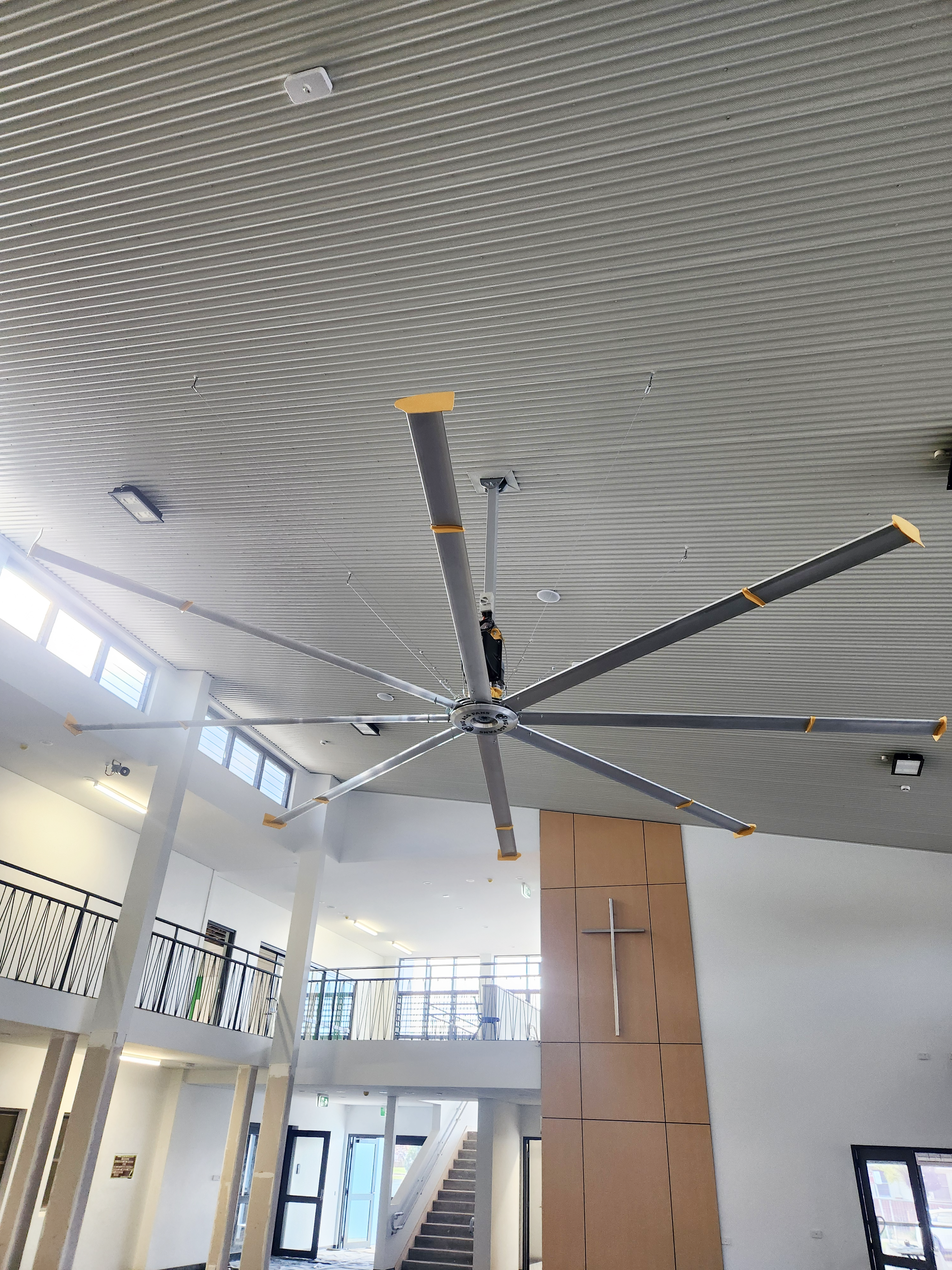 Large ceiling fan in a modern building interior with high ceilings and large windows.